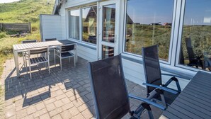 A patio with a table and chairs, large windows, and a view of a grassy field. - 10 Person Holiday Home in Harboore (Harboore)