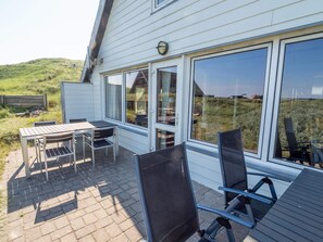 Eine Terrasse mit Tisch und Stühlen, großen Fenstern und Blick auf ein grünes Feld.