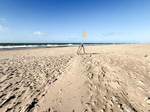 A sandy beach with footprints and a tripod with a flag. - 10 Person Holiday Home in Harboore (Harboore)