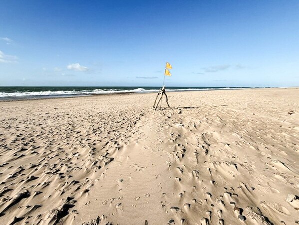 Ein sandiger Strand mit Fußabdrücken und einem Stativ mit einer Flagge.