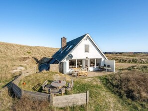 Une maison blanche avec un toit en pente, une terrasse et un espace patio aménagé avec du mobilier d’extérieur.
