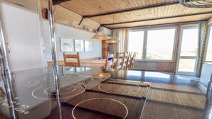 A modern kitchen with a black induction cooktop, wooden chairs, and a view of the outdoors through large windows. - 10 Person Holiday Home in Harboore (Harboore)