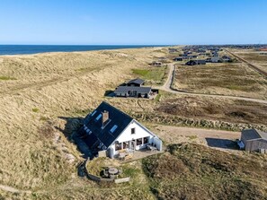 Une propriété située sur la côte, avec une maison imposante dotée d’une grande terrasse et d’un bâtiment séparé avec un toit en pente.