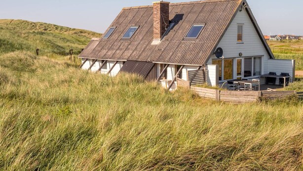 A white house with a sloped roof, a chimney, and a small porch with outdoor seating. - 10 Person Holiday Home in Harboore (Harboore)