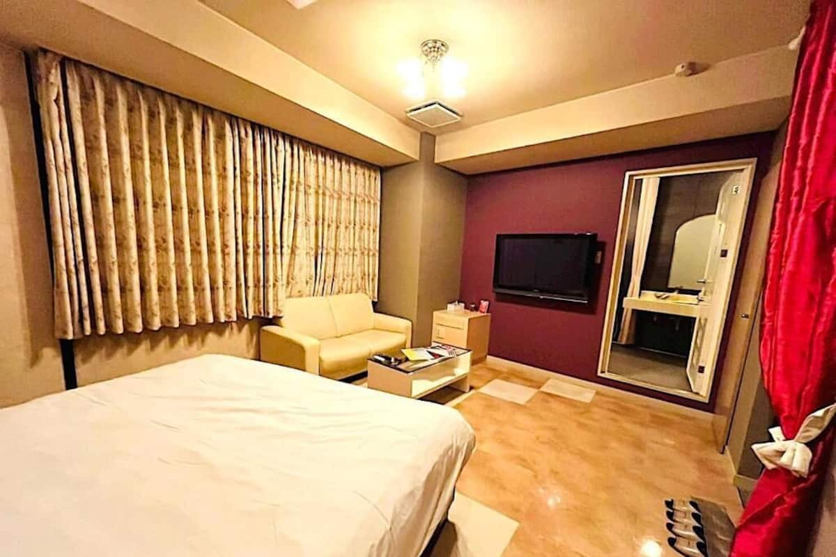 A hotel room with a bed, a sofa, a TV, a mirror, and a door.