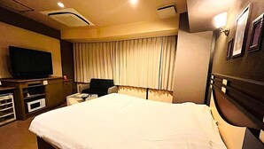 Quarto de hotel com uma cama grande, televisão, escrivaninha e janela com cortinas.