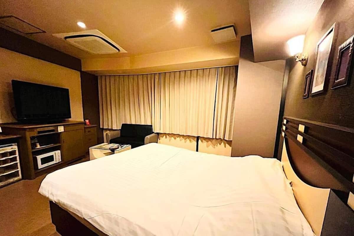 A hotel room with a large bed, a television, a desk, and a window with curtains.