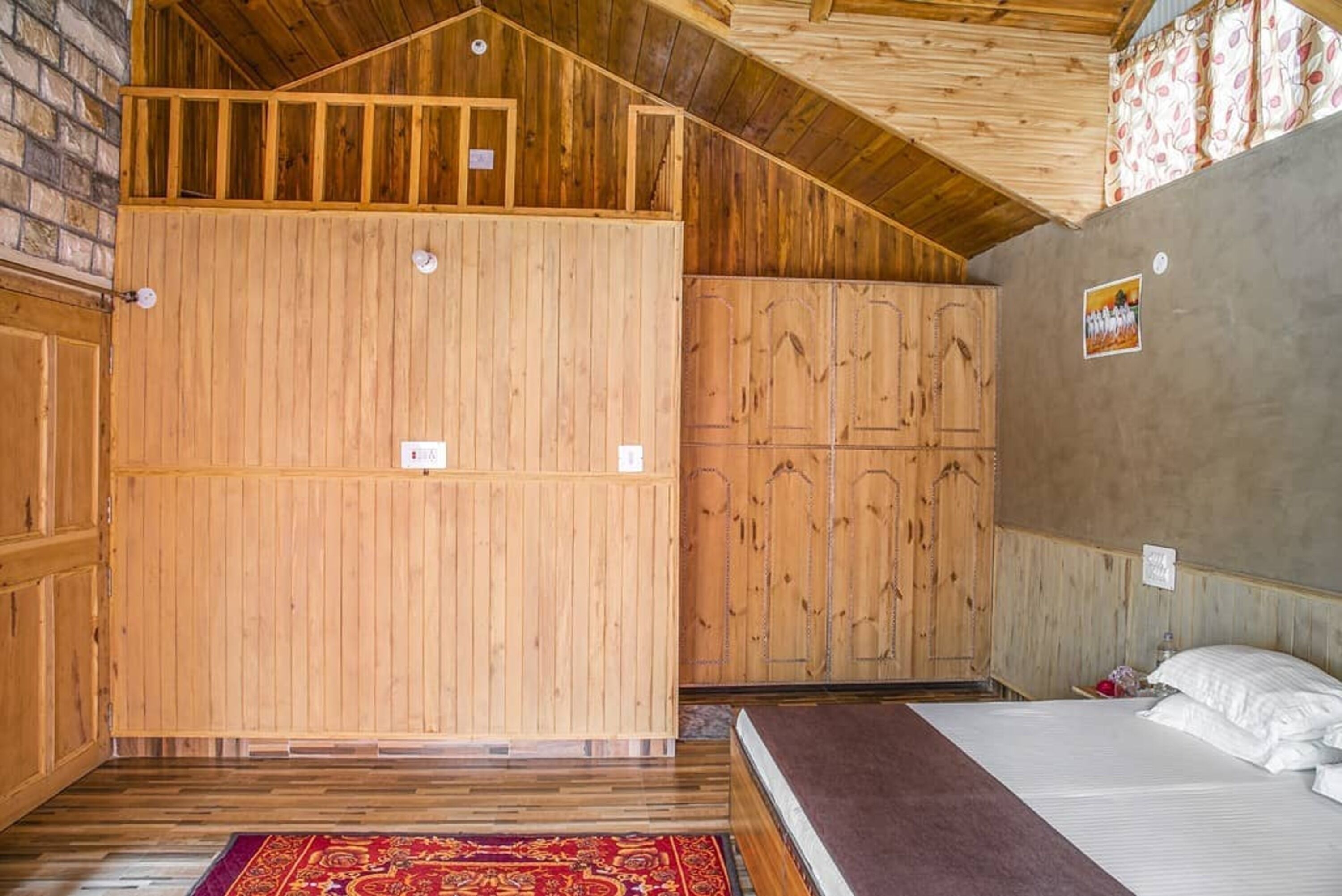 Un interior de madera con una cama, un tapete rojo estampado y paredes de madera.