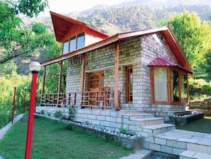 A stone house with a wooden porch, a red roof, and a view of mountains.