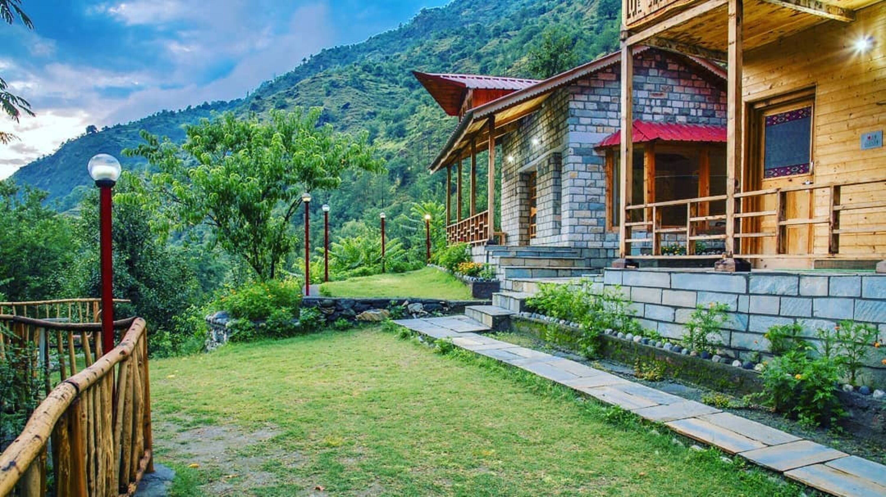 A stone building with a wooden porch, surrounded by a well-maintained garden and a mountain backdrop.