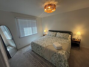 A bedroom with a bed, two bedside lamps, a bedside clock, a window with blinds, and a ceiling light fixture. - 4BR 2Bath Retreat Near Fargo Dome, MSUM, NDSU & Fargo Downtown (Moorhead)