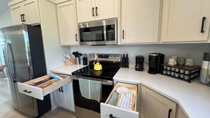 Una cocina moderna con electrodomésticos de acero inoxidable, muebles blancos y una encimera con diversos utensilios de cocina.