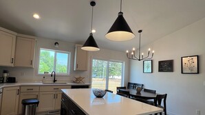 Una cocina moderna con armarios blancos, una isla grande, iluminación colgante y vistas al exterior.