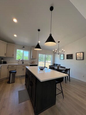 A modern kitchen with white cabinets, a large island, pendant lighting, and a view of the outdoors. - 4BR 2Bath Retreat Near Fargo Dome, MSUM, NDSU & Fargo Downtown (Moorhead)