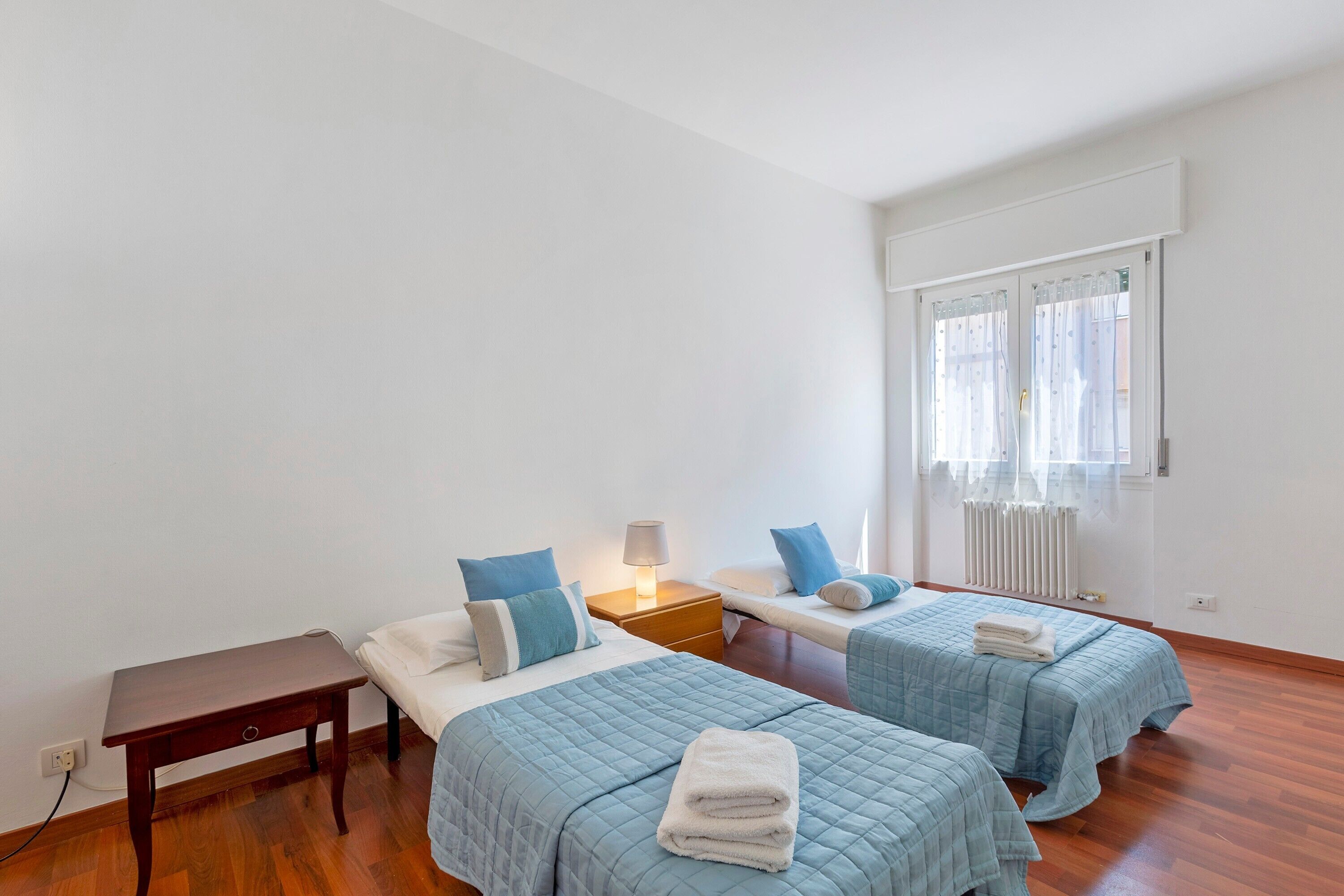 Una habitación con dos camas, una mesita, una mesilla de noche y una ventana con cortinas.