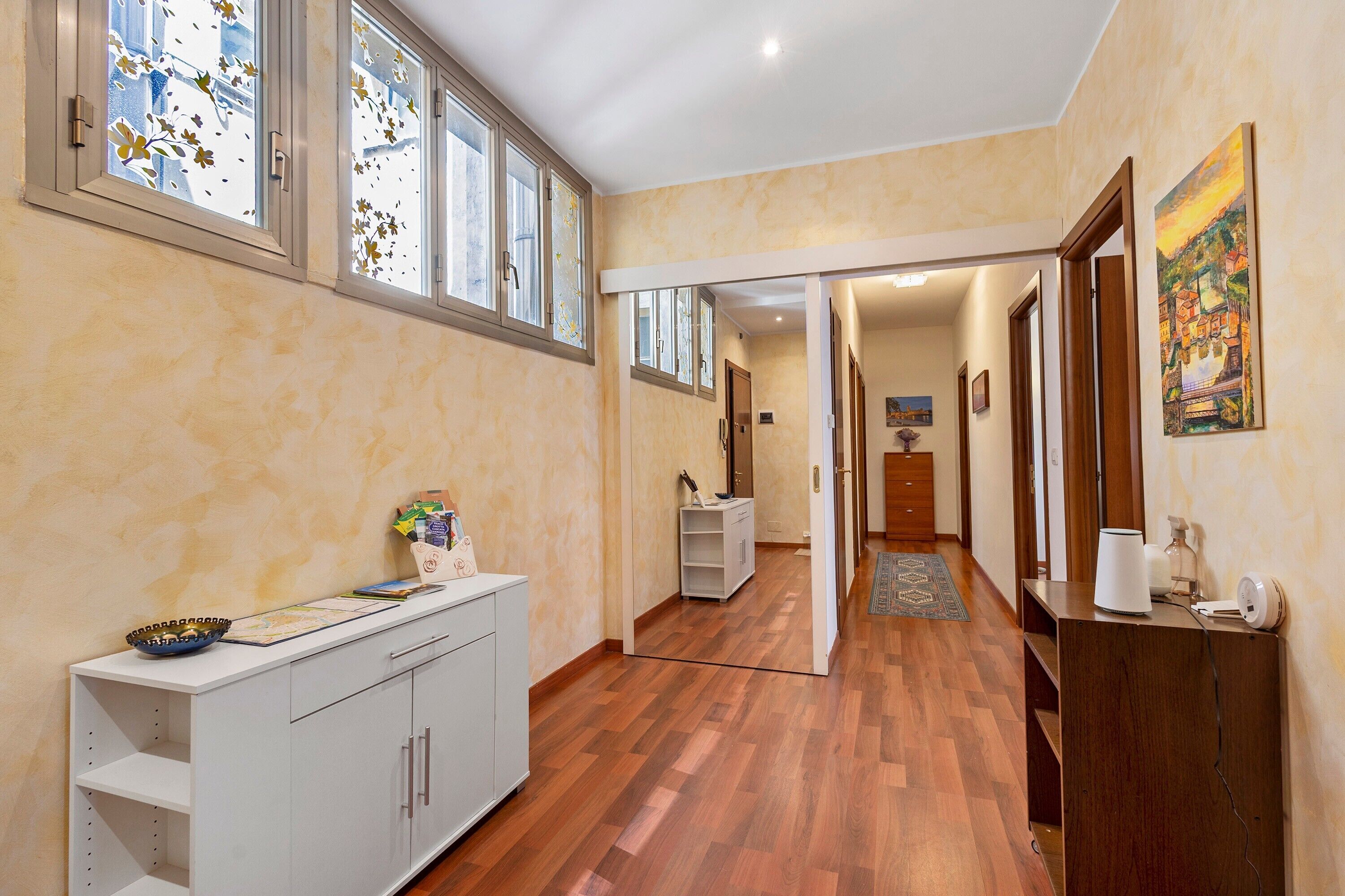 Un pasillo con piso de madera, un armario blanco y una puerta que da a otra habitación.