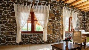A room with stone walls, wooden beams, a table, chairs, and a window with curtains.
