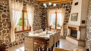 A stone-walled room with a fireplace, dining table, chairs, and a sofa.