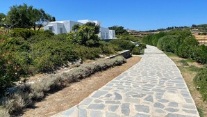 A stone pathway leading to a white building with a clear blue sky above. - A quiet Cycladic-style family home with a pool and an exceptional ocean view. (SIFNOS)