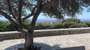 A stone wall with a tree in the foreground and a view of the sea and hills in the background. - A quiet Cycladic-style family home with a pool and an exceptional ocean view. (SIFNOS)