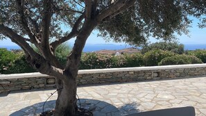 A stone wall with a tree in the foreground and a view of the sea and hills in the background. - A quiet Cycladic-style family home with a pool and an exceptional ocean view. (SIFNOS)