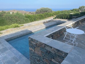 A stone pool with a white table and chairs, surrounded by stone walls and a view of the ocean. - A quiet Cycladic-style family home with a pool and an exceptional ocean view. (SIFNOS)