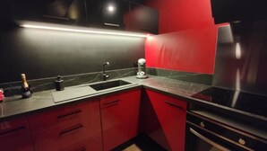 Een moderne keuken met rode kastjes, een zwart aanrecht en roestvrijstalen apparatuur.