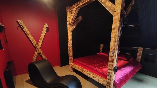 Een kamer met een houten baldakijnbed, een zwarte fauteuil en een rode wand.