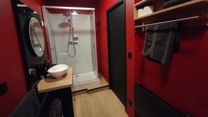 Een kleine badkamer met een douche, wastafel, spiegel en handdoekhouder.