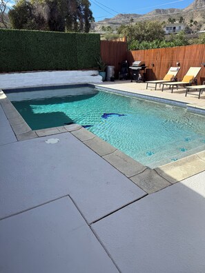 Ein rechteckiger Swimmingpool mit klarem, blauem Wasser, umgeben von einem Holenzaun und einer weißen Mauer.