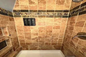 A bathroom with a tiled shower wall, a white bathtub, and a wall-mounted faucet. - Unplug & Unwind - Cozy Alpine A-Frame Tucked Away in the Arizona Pines (Flagstaff)