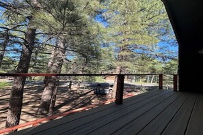 Eine Holzterrasse mit Geländer, umgeben von hohen Kiefern.