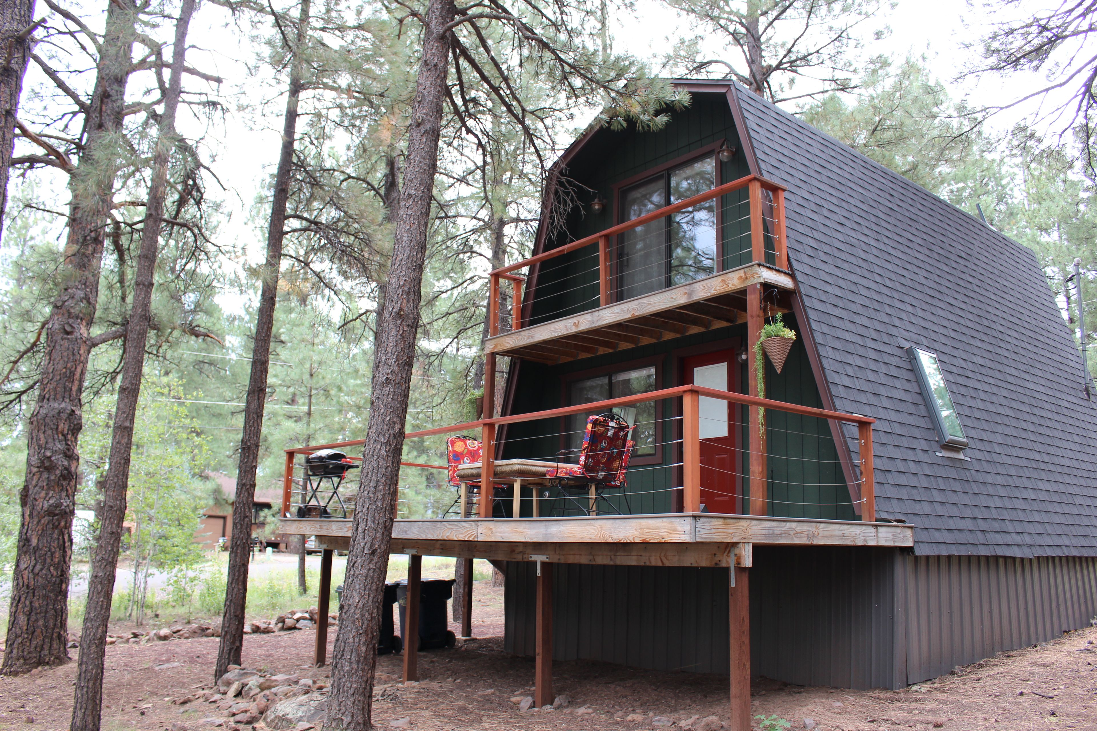 A cabin with a wooden deck and a balcony, surrounded by trees.