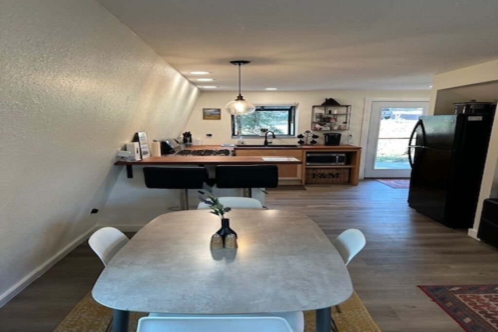 A modern kitchen with a dining area, wooden cabinets, and a black refrigerator.