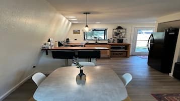 A modern kitchen with a dining area, wooden cabinets, and a black refrigerator.