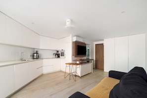 A modern kitchen with white cabinets, a built-in oven, and a coffee machine.