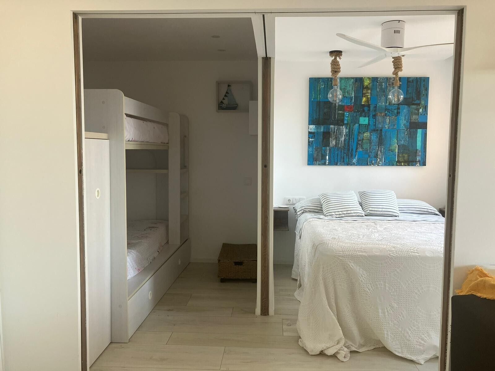 Una habitación con literas, una cama con almohadas a rayas, un ventilador de techo y una obra de arte en la pared.