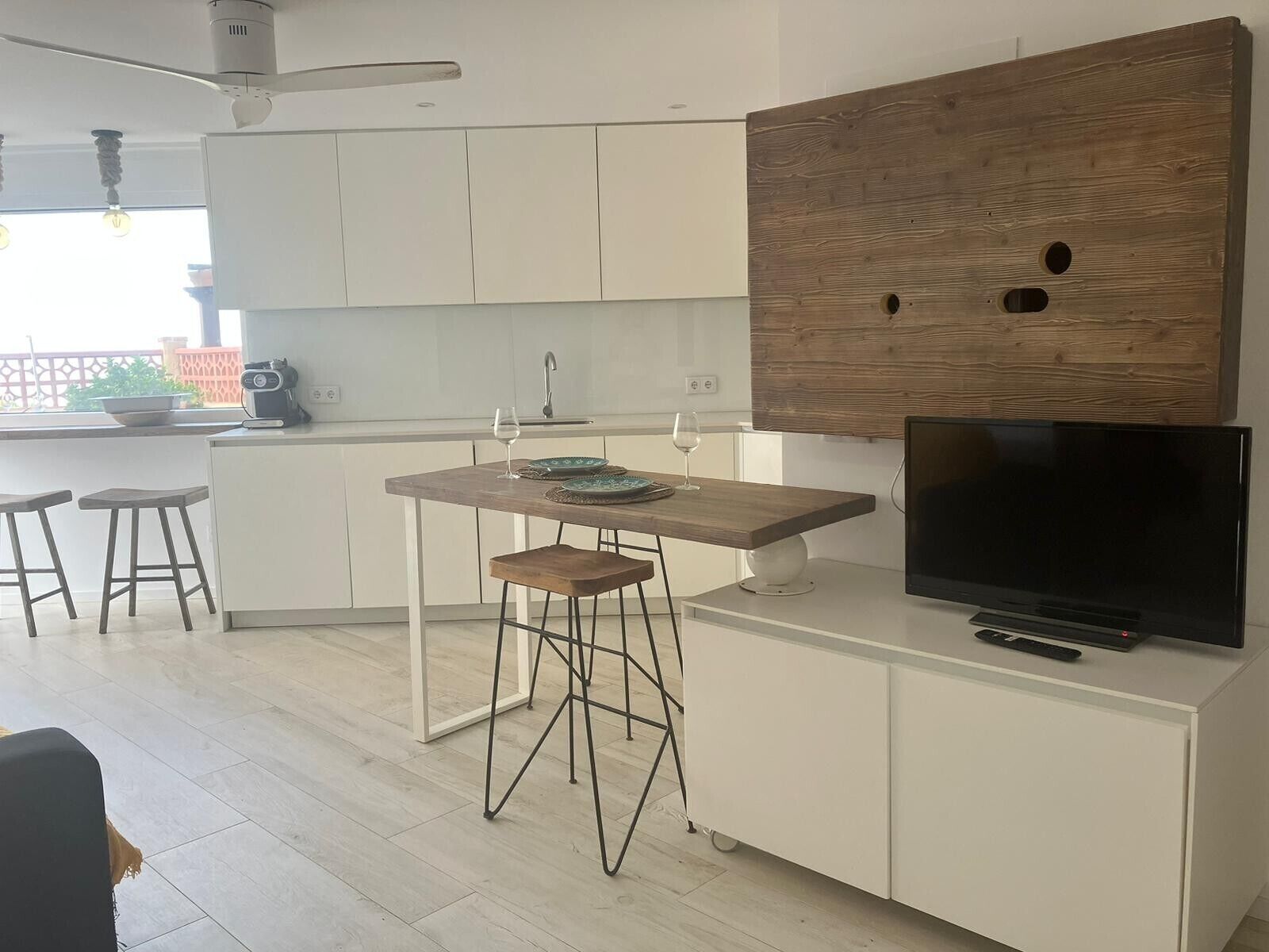 Eine moderne Küche mit einem Holztisch, Barhocker, einem Fernseher und einem Deckenventilator.
