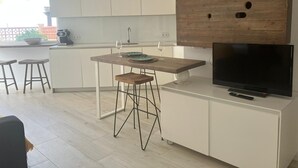 Una cocina moderna con una mesa de madera, taburetes de bar, un televisor y un ventilador de techo.