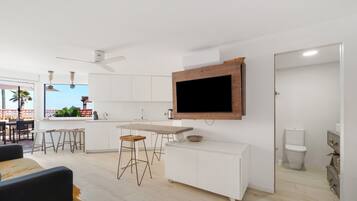 A modern kitchen with a flat-screen TV, white cabinetry, and a dining area with bar stools.