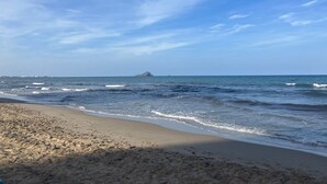 Una playa con olas, cielo despejado y una isla a lo lejos.