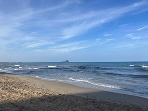 Ein Strand mit Wellen, einem klaren Himmel und einer fernen Insel.