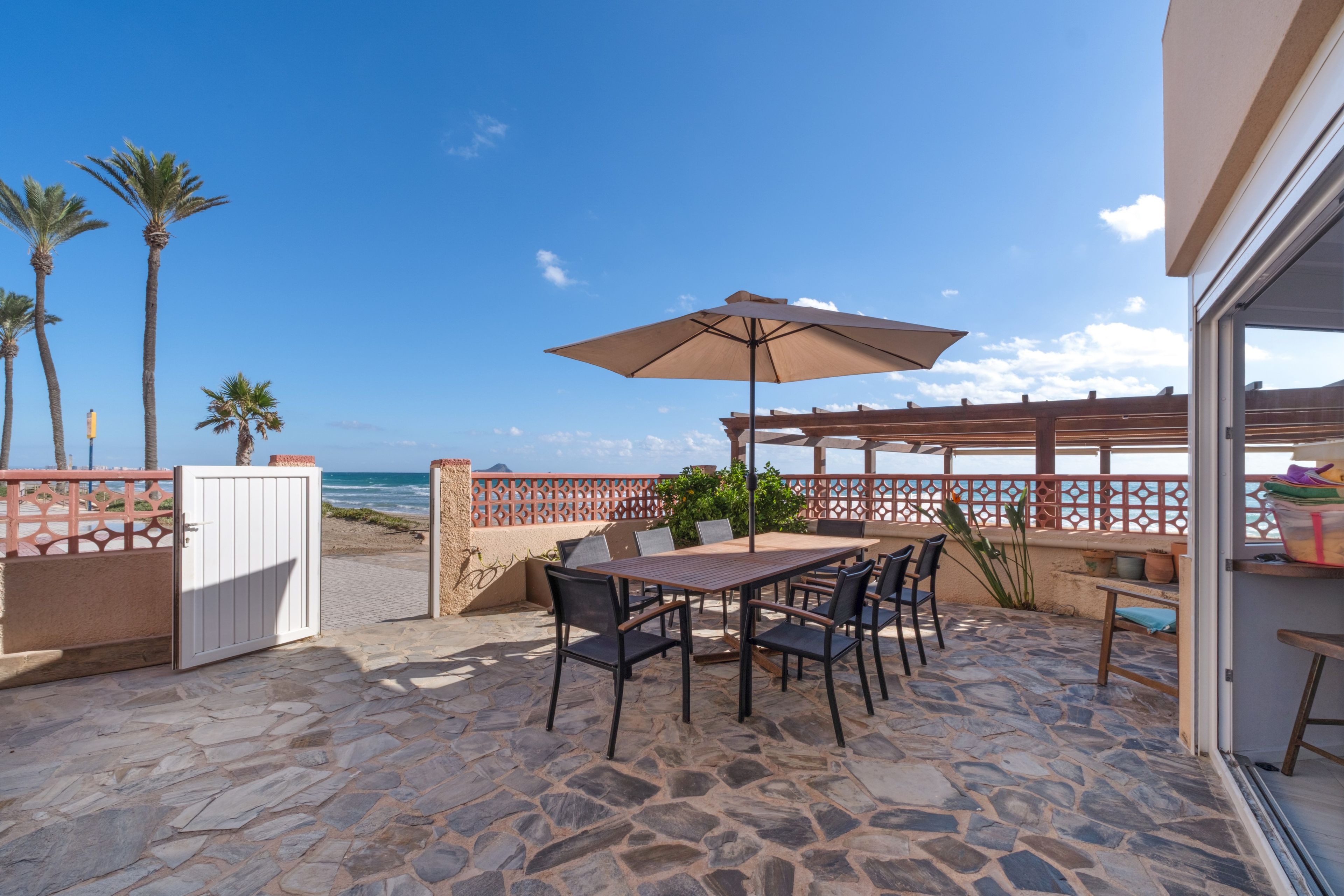 Eine Außenpatio mit Tisch und Stühlen, einer Holz-Pergola und Blick auf Strand und Meer.