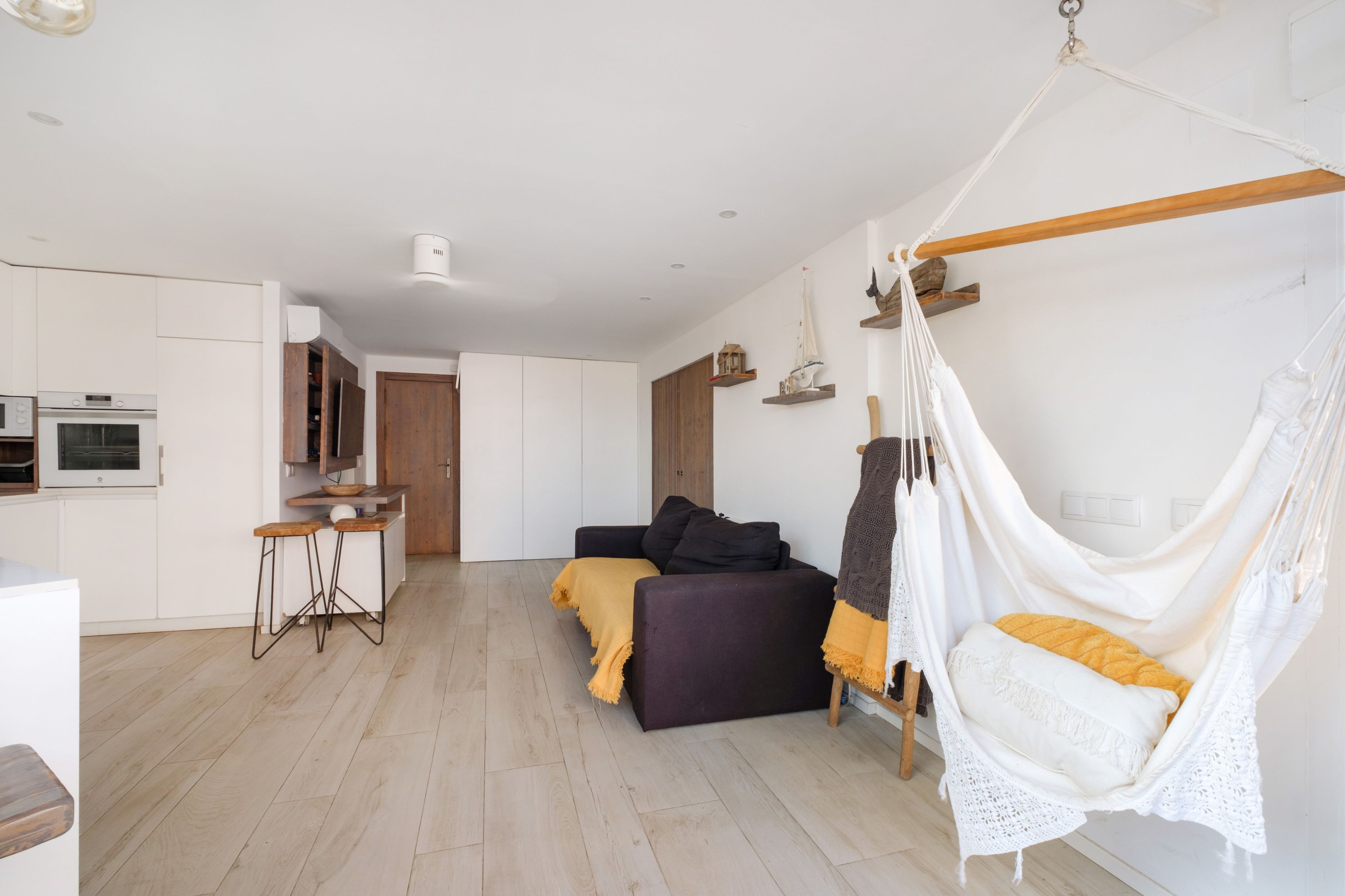 Une chambre à coucher moderne et minimaliste, avec un lit, un fauteuil suspendu et une petite kitchenette.
