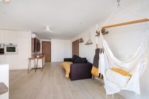 Une chambre à coucher moderne et minimaliste, avec un lit, un fauteuil suspendu et une petite kitchenette.