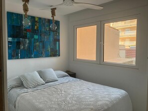 Ein Schlafzimmer mit einem Bett, einem Fenster mit Blick, einem Deckenventilator und einem blauen, abstrakten Gemälde.