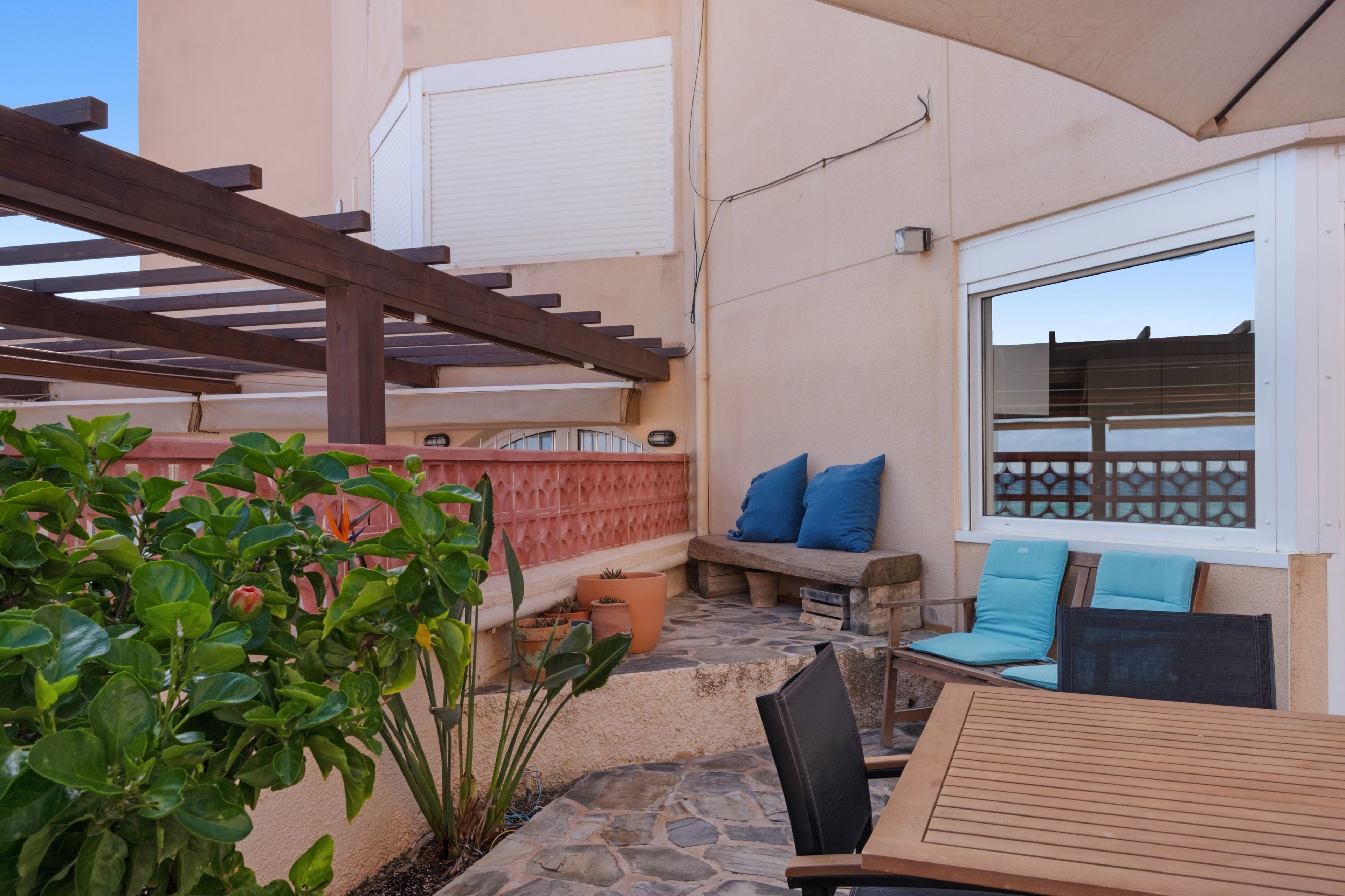 Eine Terrasse mit einem Holztisch, blauen Kissen und einem Steinboden.
