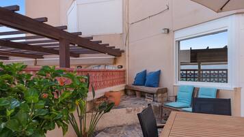 Eine Terrasse mit einem Holztisch, blauen Kissen und einem Steinboden.