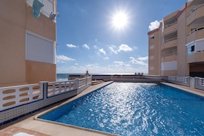 A swimming pool with a view of the sea, surrounded by buildings with balconies.