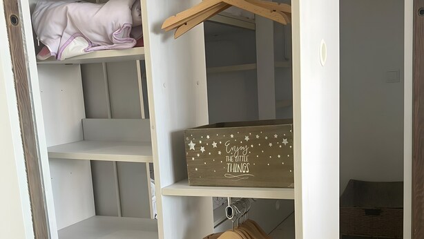 Un armario blanco con varios estantes, una barra para colgar y un caja de madera decorada con estrellas.